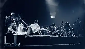 A quartet performs acoustic music to the audience while being covered by a dark stage-light.