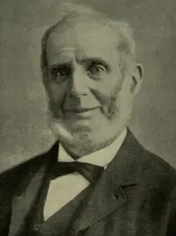 Portrait photograph of an older man with a receding hairline and prominent sideburns, wearing a dark jacket, waistcoat, white shirt, and bow tie, facing the camera.