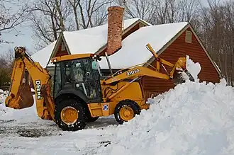 A backhoe with a snow plow attachment clearing snow