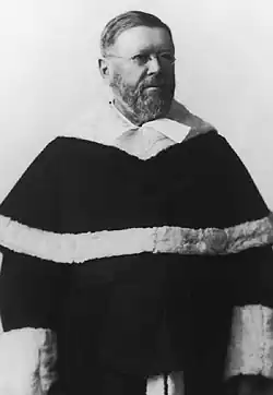 A black and white photograph of a man standing wearing a judicial robe.