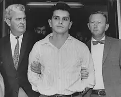 Black and white photo of Patler, surrounded by two detectives