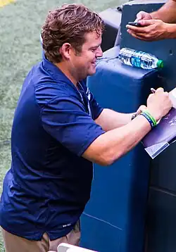 Candid waist-up photograph of Schneider wearing a blue shirt and signing an autograph.
