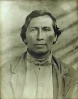 John Solomon with short, dark hair wearing a single-breasted jacket and a neckerchief
