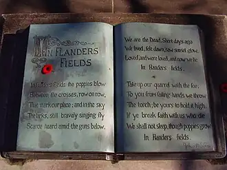A sculpture in the form of an open book. The text of the poem "In Flanders Fields" is written within and a small red poppy lies on top.