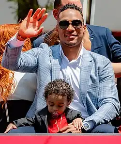 Jorge Polanco, wearing a suit and sunglasses and with a small child in his lap, waving from the bed of a red pickup truck