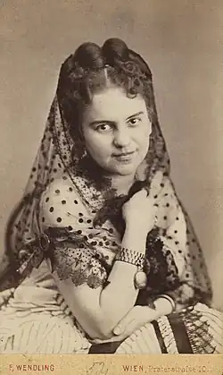 Photograph of a young woman with pinned up hair wearing a white dress and a partially transparent scarf