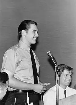 Black and white photo of Tommasi standing up and giving a speech