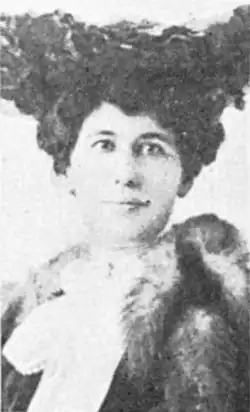 A white woman with dark hair, wearing a dark hat and a fur collar