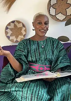 Bae sits on purple couch with green dress, screen shot from A Little Juju Podcast