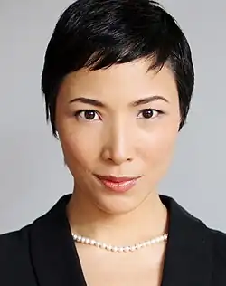 close-up of Julee Cerda wearing a black, open-necked top and pearl necklace, looking directly at camera with slight smile