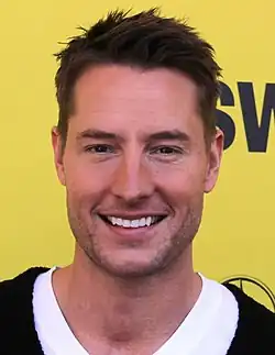 A man with dark hair smiling at the camera in front of a yellow background.