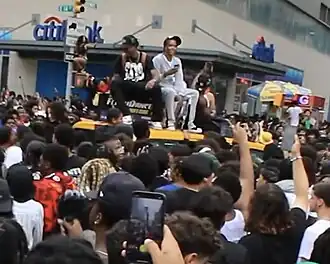 Large crowd at Union Square with two people sitting on a car and a woman standing on a headlight