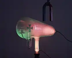 When the magnet is reversed, it bends the rays down, so the green spot is lower. The pink glow is caused by cathode rays striking residual gas atoms in the tube.