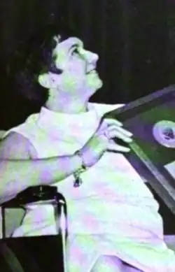 Smiling white woman with short dark hair, seated in a wheelchair, holding an award plaque