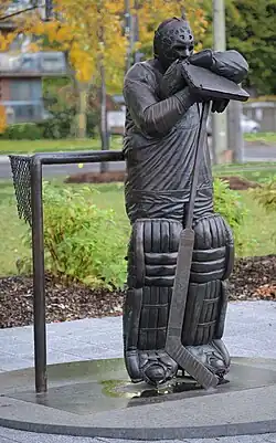 Bronze statue of an ice hockey netminder standing while leaning on a hockey stick