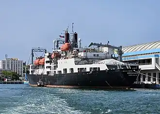 Kennedy in Texas A&M insignia moored to Pier 4 (cruise terminal) with pilot disembarking in San Juan Harbor, San Juan, Puerto Rico (July 2023)
