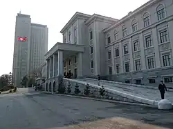 The entrance of Kim Il Sung University in Pyongyang. A tower block and a North Korean flag are in the distance.