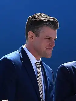 Headshot of Kinsley in a suit against a blue background