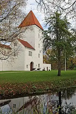 A large, whitewashed medieval castle with a prominent tower, surrounded by a moat.