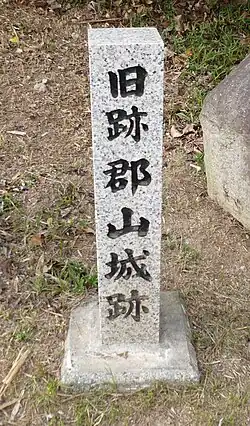 A vertical, light gray, granite squared post with Japanese writing carved into the surface.