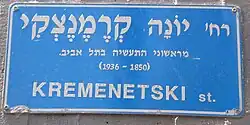 The blue Israeli street sign is in Hebrew. Translated to English it says: "Yonah Kremenetski, one of the first industrialists in Tel Aviv (1850–1936)."