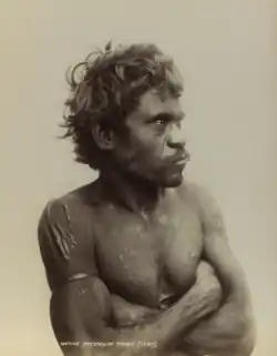 Portrait photograph of a shirtless Aboriginal man with crossed arms.