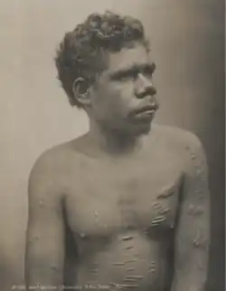 Portrait photograph of a shirtless Aboriginal man with a scarred torso