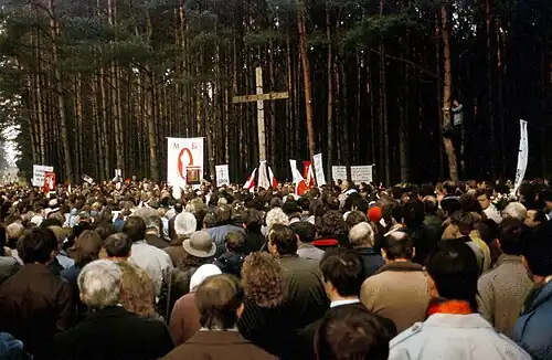 Crowds gathering in front of a cross in a forest; Kurapaty, Belarus, 1989