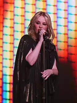 Photograph of Minogue dressed in black singing onto a microphone
