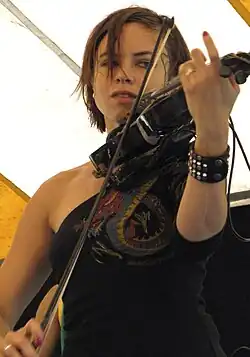 Kytami wearing a black, patterned, sleeveless top, playing violin onstage