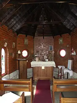 Small room with brick walls, pews, and a small altar