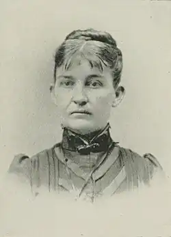 19th-century B&W portrait photo of a woman with her hair in an up-do, wearing a dark, fitted blouse.