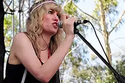 A woman wearing a black singlet and pink hairband, singing into a microphone