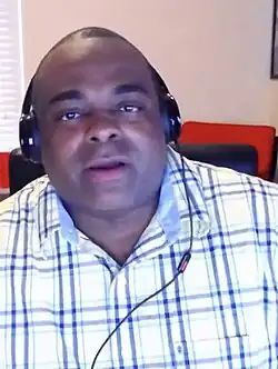 A man with short hair wearing a blue-and-white t-shirt and headphones.