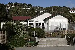A small wooden building with white walls. In front of it is a small garden