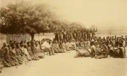 Lewanika (looking at the camera) sits on a chair with dozens of others kneeling to his left and right. A handful of drummers and a silimba (xylophone) player sit opposite him and them.