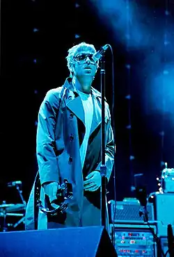 A male singing into a microphone and playing a tambourine on a stage.