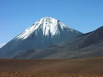 A snow-capped cone rises from a desolate landscape