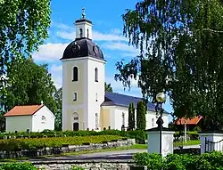 A white church in Lit, one story with a two-story tower with a golden cross on top.