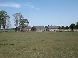 Photograph of a large grassy field with buildings in the background