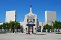 Photograph of the peristyle gate of the Los Angeles Memorial Coliseum, tile mosaicon the underside of the arch, and the Olympic torch reaching to the blue sky.