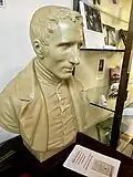 Louis Braille has short, curly hair and he is wearing a jacket.
