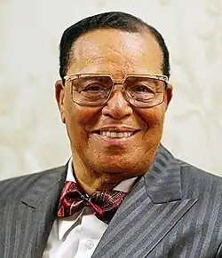 An elder black man with short cropped black hair, wearing glasses, looking out towards the viewer. He is wearing a white shirt, gray suit jacket, and red bowtie.