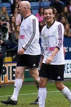 Two men walking together on a football field, wearing a black and white football kit.