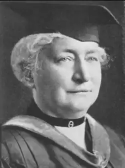 A white woman with white hair, wearing academic cap and gown