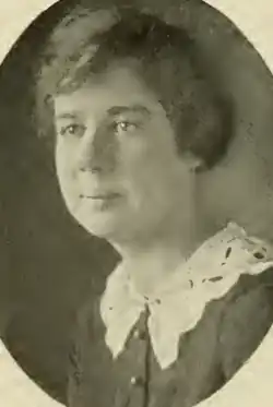 A young white woman with side-parted hair, wearing dark blouse with a white lace collar