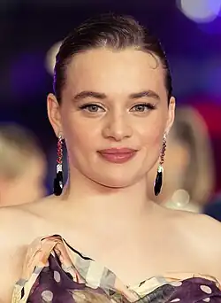 close-up of Luna Wedler wearing a patterned strapless top, smiling directly at camera