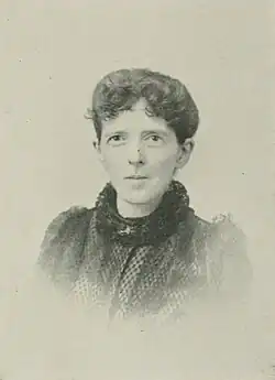 B&W portrait photo of a young woman wearing a dark, high-collared blouse with her hair in an up-do.