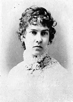19th-century B&W portrait photo of a woman with her hair in an up-do, wearing a dark, fitted blouse.