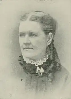 19th-century B&W portrait photo of a woman with her hair in an up-do, wearing a dark, fitted blouse.
